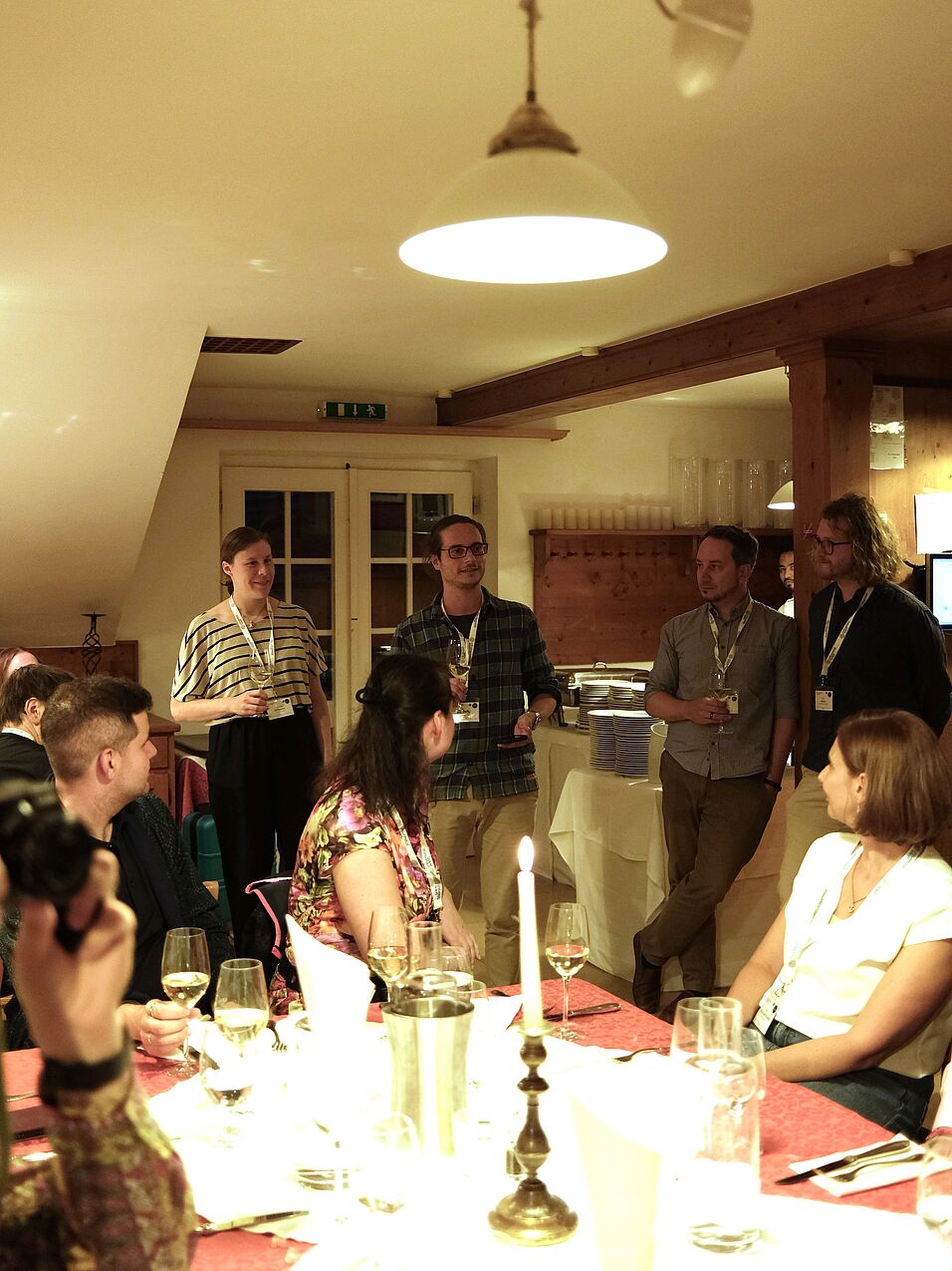 Mehrere Personen in einer Gasthausstube - teilweise sitzend, teilweise stehend. Eine Person hält eine Ansprache. 